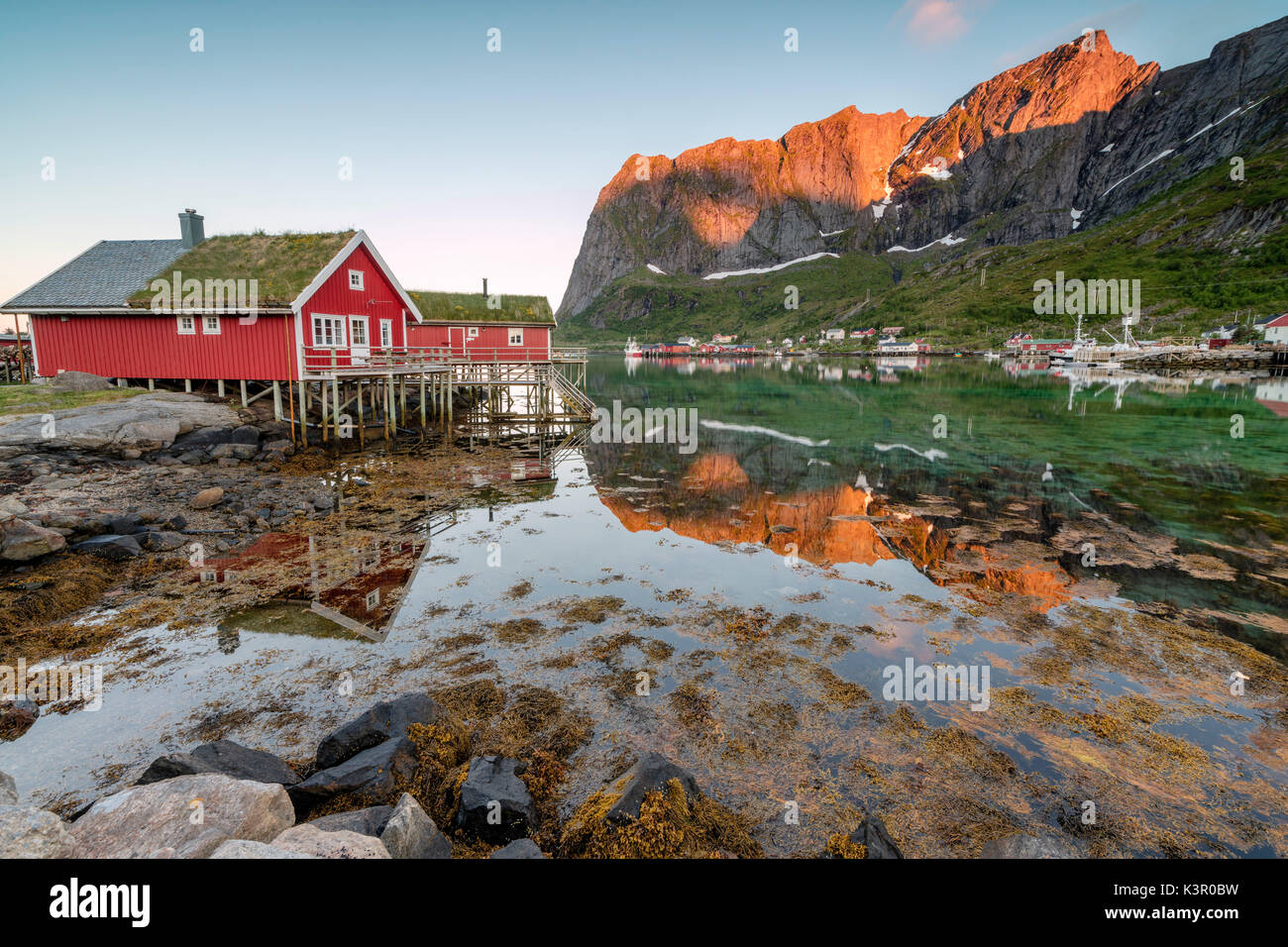 Village de pêcheurs et les pics reflètent dans l'eau sous le soleil de minuit Reine Nordland County Lofoten, Norvège du Nord Europe Banque D'Images