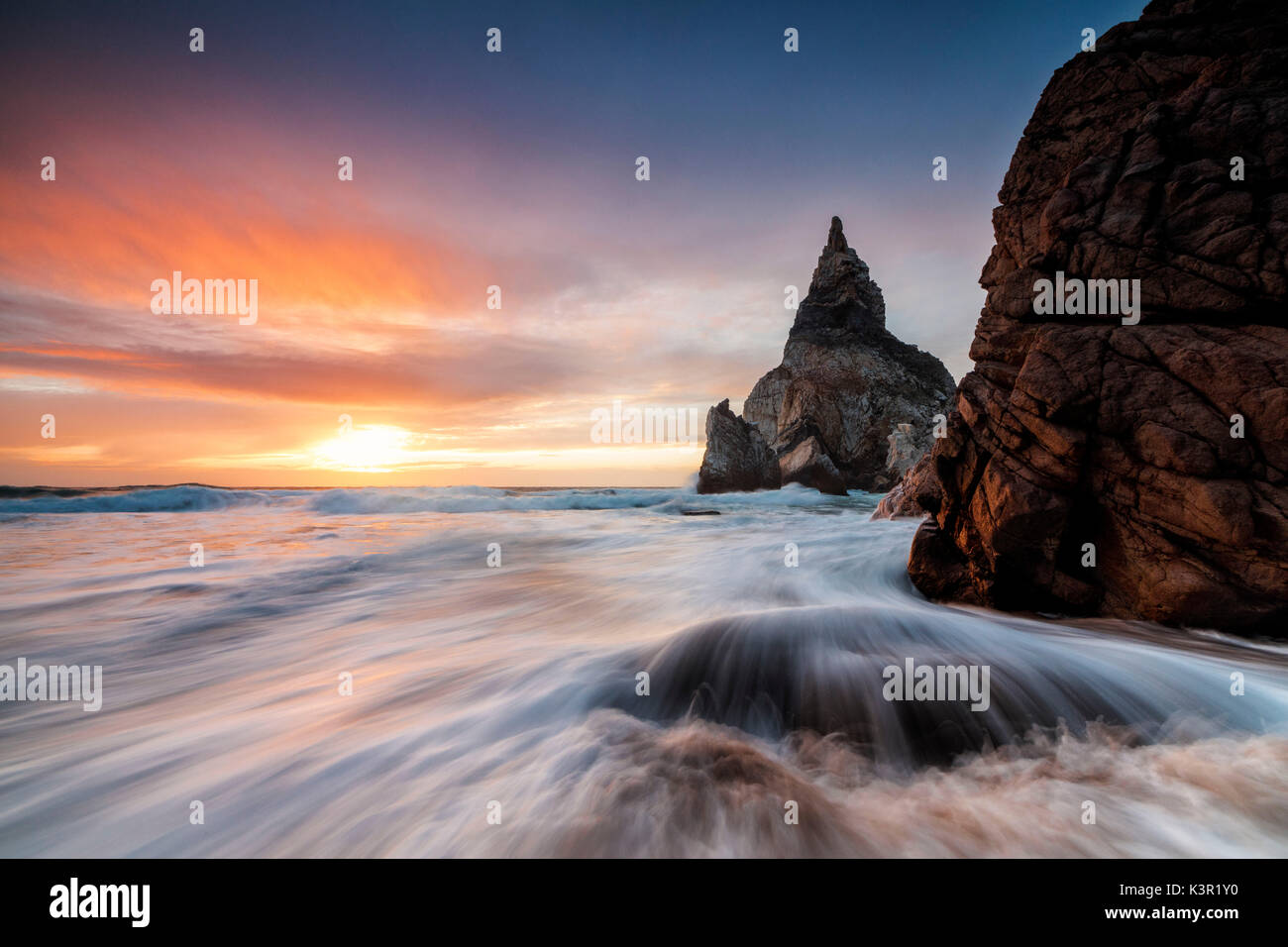 Le Fiery sky au coucher du soleil se reflète sur les vagues de l'océan et les falaises Praia da Ursa Cabo da Roca Colares Sintra Portugal Europe Banque D'Images