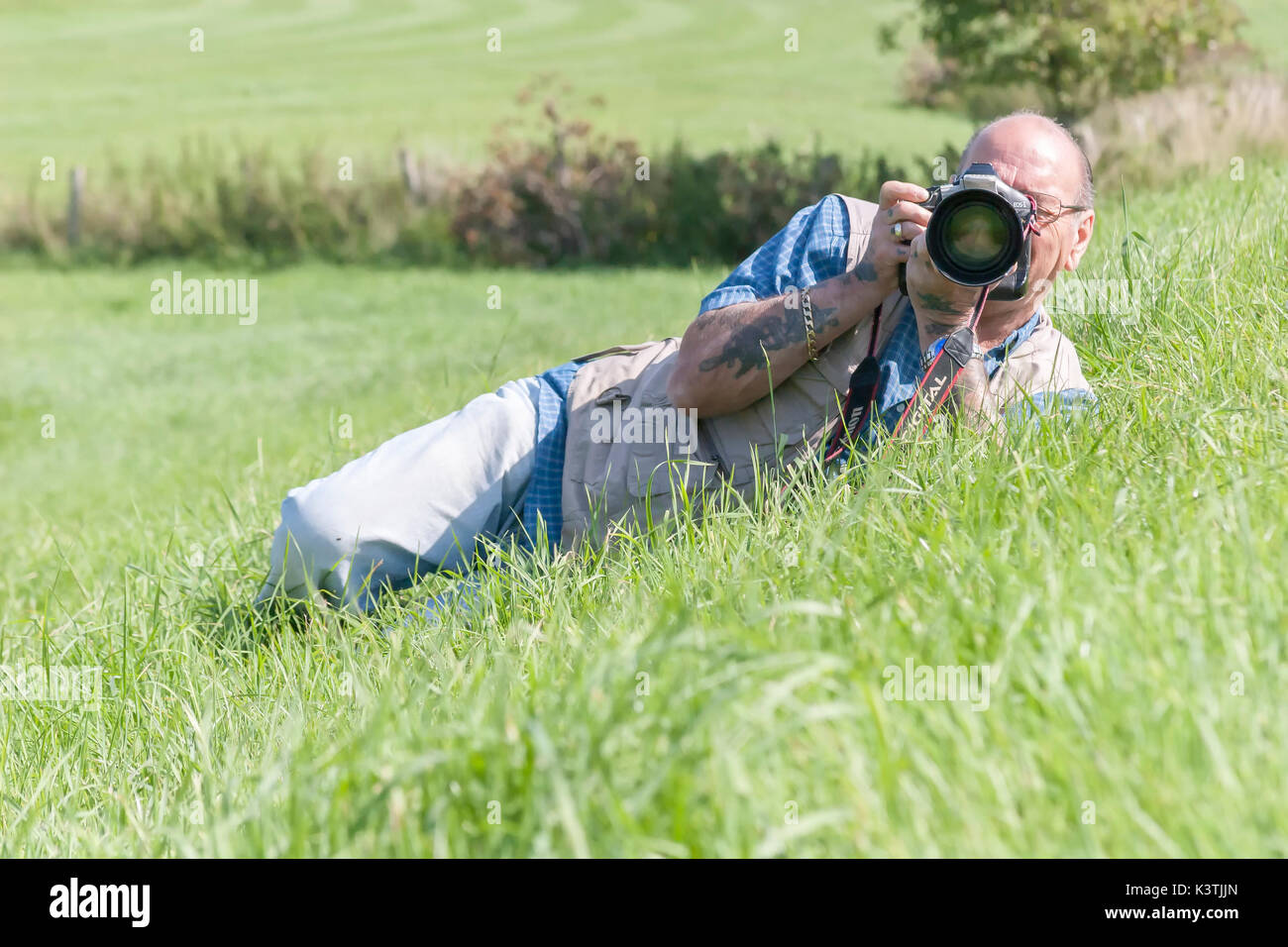 Homme portant sur une banque d'herbe de prendre des photos, à l'aide d'un appareil photo Canon. Banque D'Images