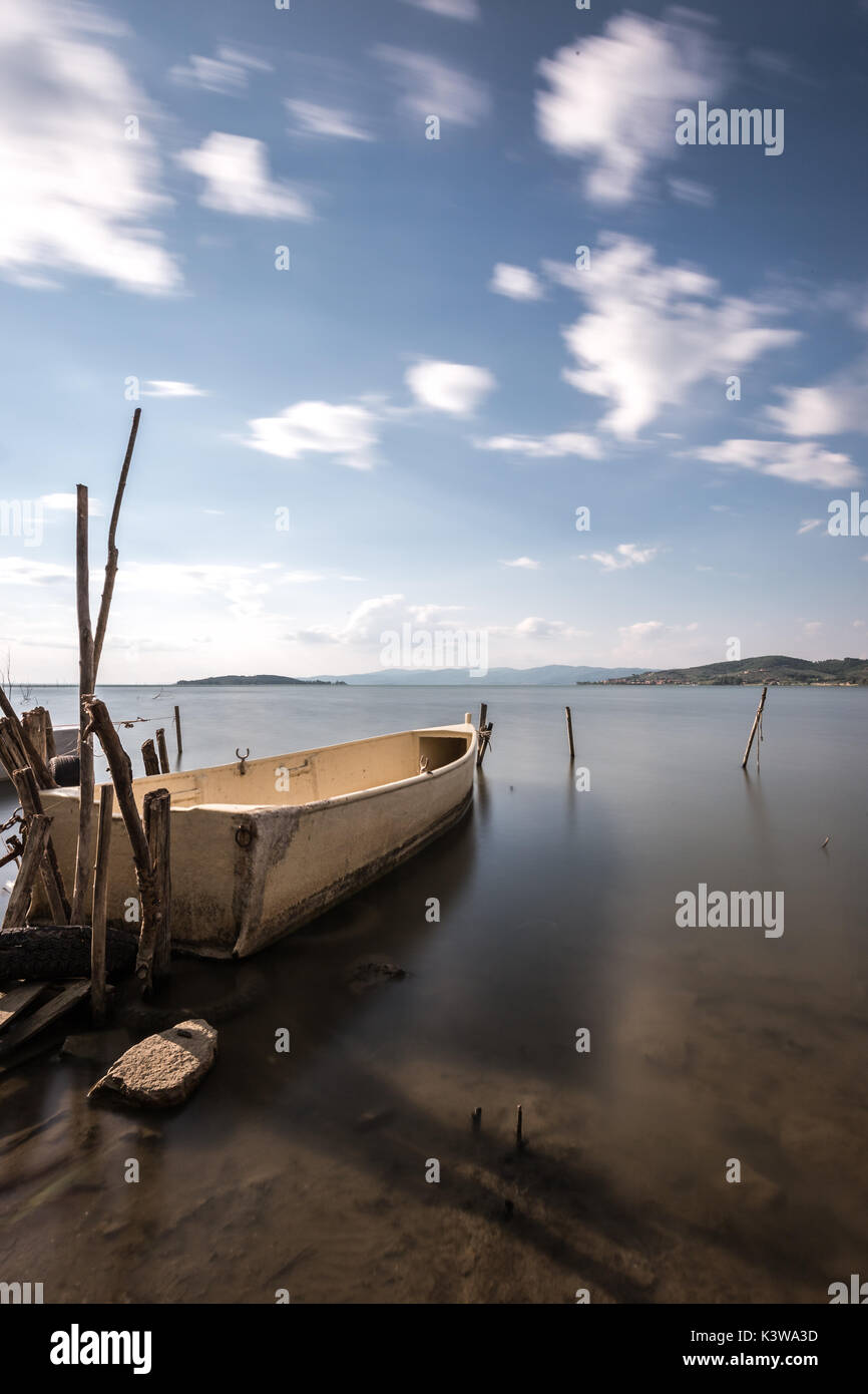 Un petit bateau de pêche sur un lac, avec de l'eau parfaitement immobile et nuages en mouvement Banque D'Images