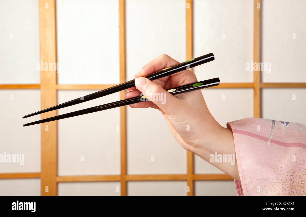 La main avec baguettes holding manche kimono japonais en face de la fenêtre coulissante shoji Banque D'Images