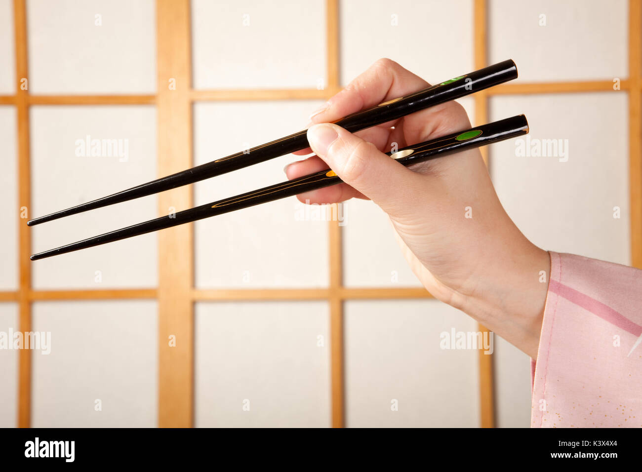 Dans les mains des baguettes manche kimono tenant en face d'une fenêtre coulissante shoji japonais Banque D'Images