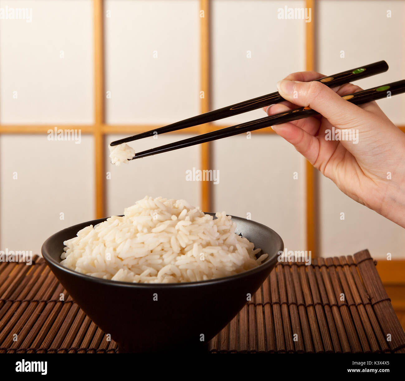 Mains tenant le riz avec des baguettes en face d'une fenêtre coulissante shoji japonais Banque D'Images