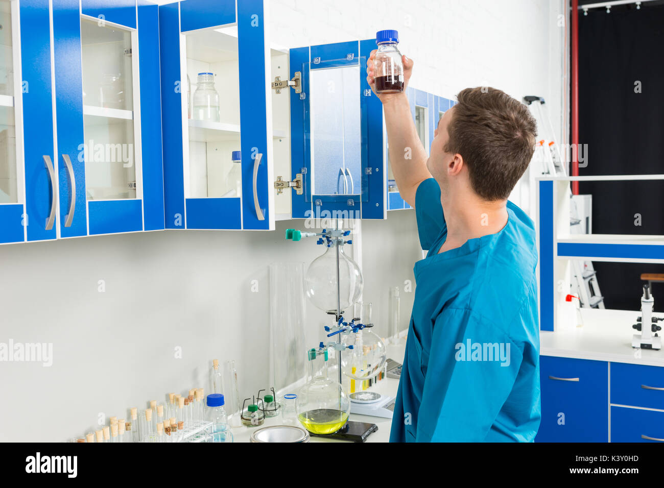 Jeune scientifique en uniforme est à la recherche de bouteille avec une substance chimique dans un laboratoire. concept de la santé et des biotechnologies Banque D'Images