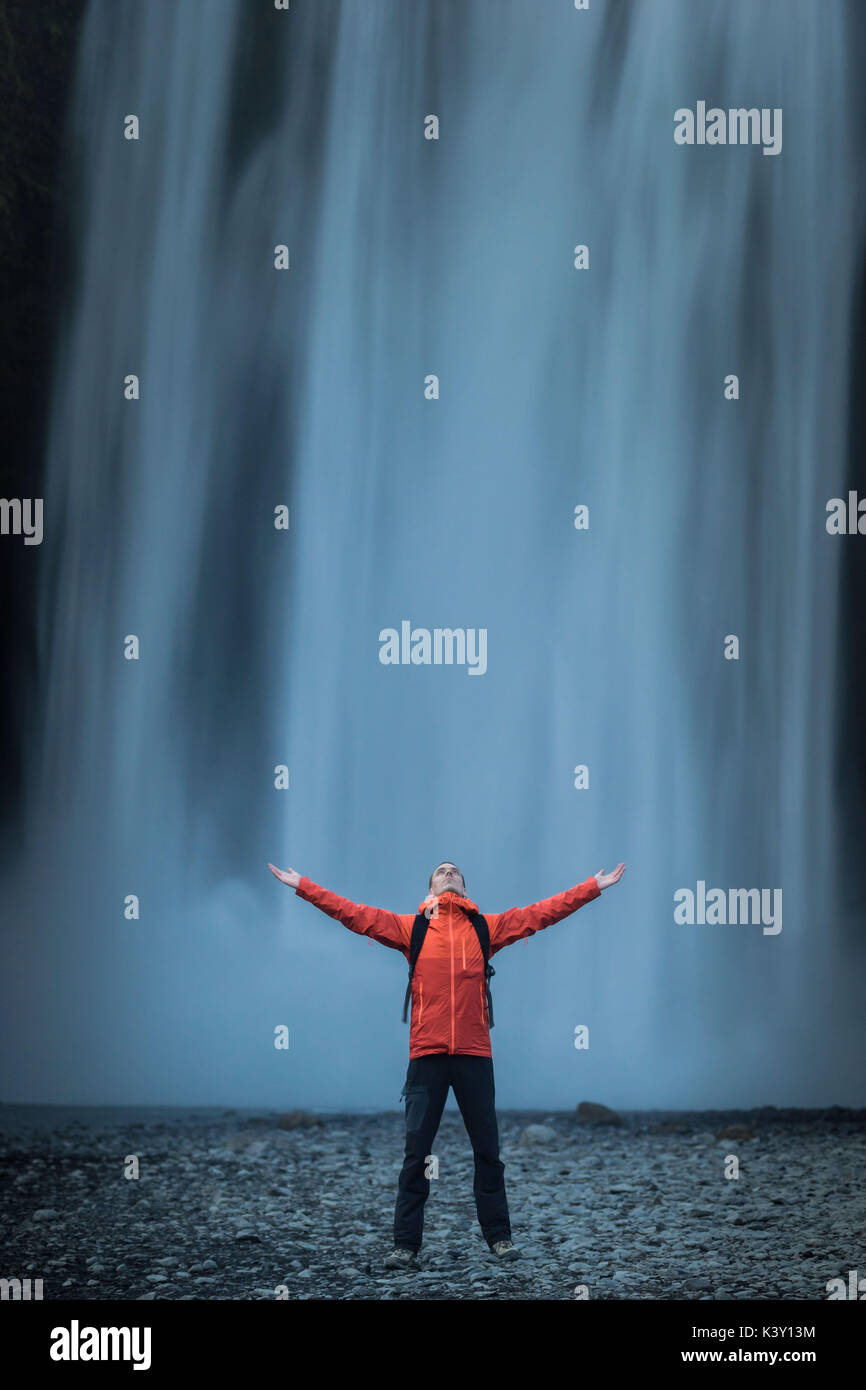 Homme dans un manteau orange standing in front of Skogafoss chute d'eau, de l'Islande. Banque D'Images