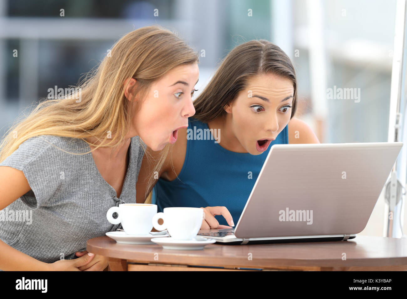 Deux amis surpris à regarder le contenu scandaleux dans un ordinateur portable assis dans un bar Banque D'Images