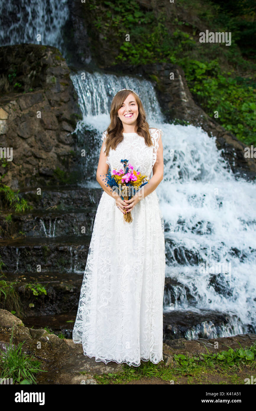 Bride holding bouquet de mariage coloré en face d'une cascade Banque D'Images