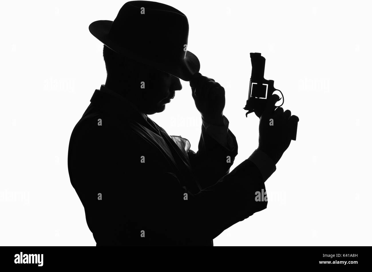Silhouette d'un détective privé avec un pistolet dans la main droite. Ressemble à gangster Al Capone mafieux et rester d'un côté à l'appareil photo. Il porte une veste de PPC. Poli Banque D'Images Silhouette d'un détective privé avec un pistolet dans la main droite. Ressemble à gangster Al Capone mafieux et rester d'un côté à l'appareil photo. Il porte une veste de PPC. Poli Banque D'Images