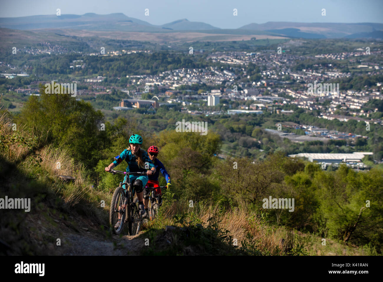 Un vélo de montagne femmes mène un homme une montée au Bikepark de galles avec la ville de Merthyr Tydfil et les Brecon Beacons dans l'arrière-plan. Banque D'Images