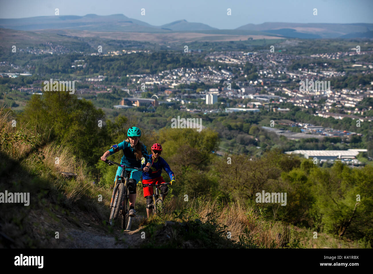 Un vélo de montagne femmes mène un homme une montée au Bikepark de galles avec la ville de Merthyr Tydfil et les Brecon Beacons dans l'arrière-plan. Banque D'Images