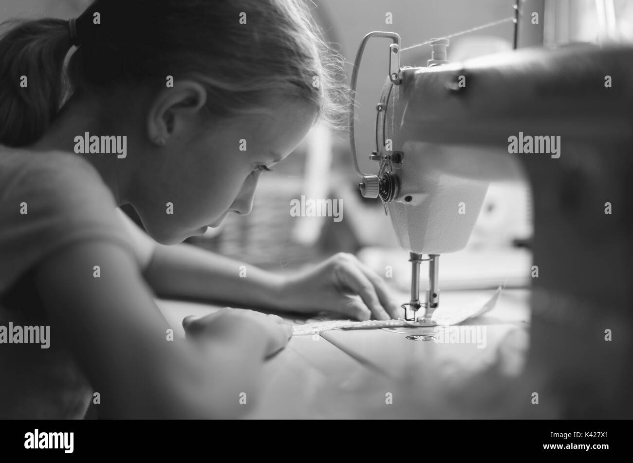 Petite fille travaillant sur machine à coudre à la maison. Noir et blanc. Banque D'Images