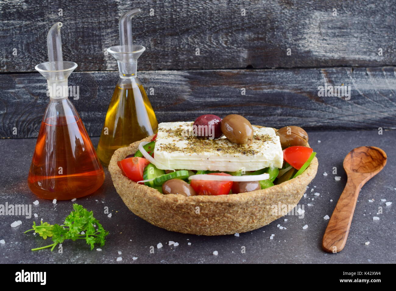 Salade grecque traditionnelle avec le concombre, l'oignon, tomate, paptika, fromage feta, l'huile d'olive et l'origan dans un bol avec du seigle comestibles en pots de verre avec de l'huile d'olive , le vinaigre et des olives sur un fond abstrait Banque D'Images