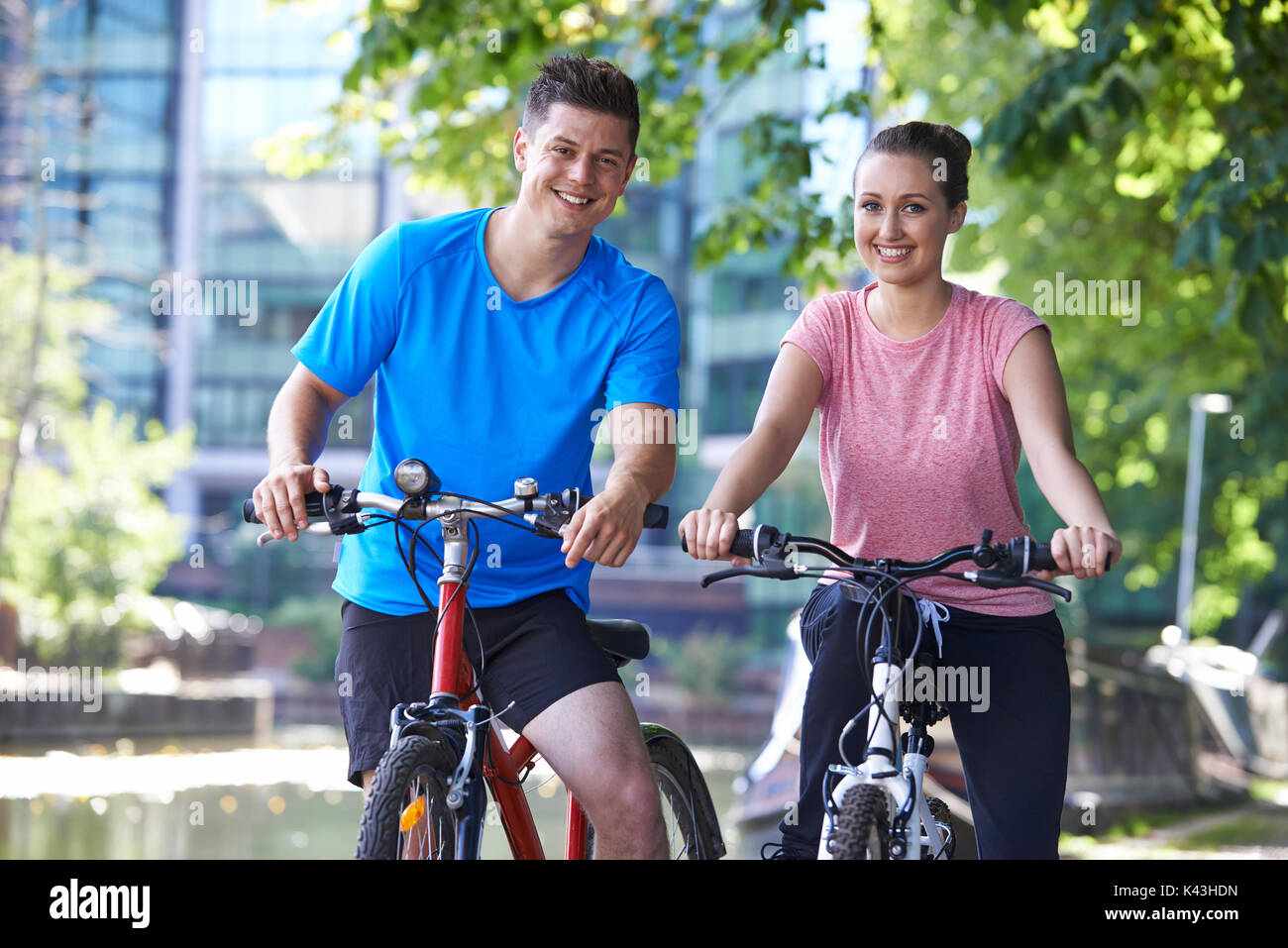 Jeune couple à vélo à côté de rivière en milieu urbain Banque D'Images