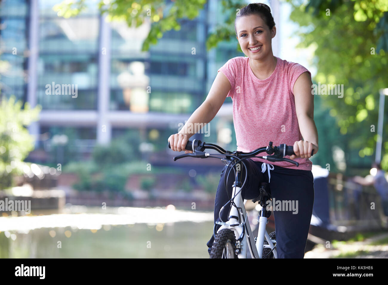 Jeune Femme à vélo à côté de rivière en milieu urbain Banque D'Images