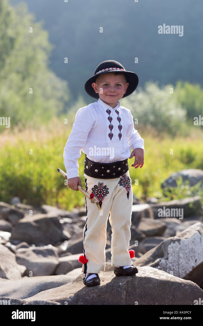 Garçon enfant souriant dans la montagne polonaise traditinal Costume et chapeau noir se dresse sur les rochers des montagnes. Portrait complet du corps vertical Banque D'Images