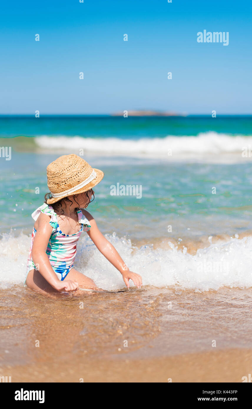 Petite fille, enfant avec chapeau de paille et floral maillot de face à la mer dans une journée ensoleillée Banque D'Images