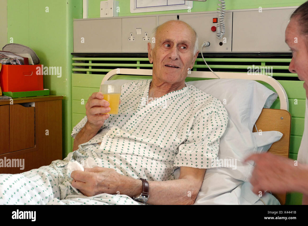 Un homme âgé souffrant de démence couché dans un lit d'hôpital souriant à son visiteur. Banque D'Images