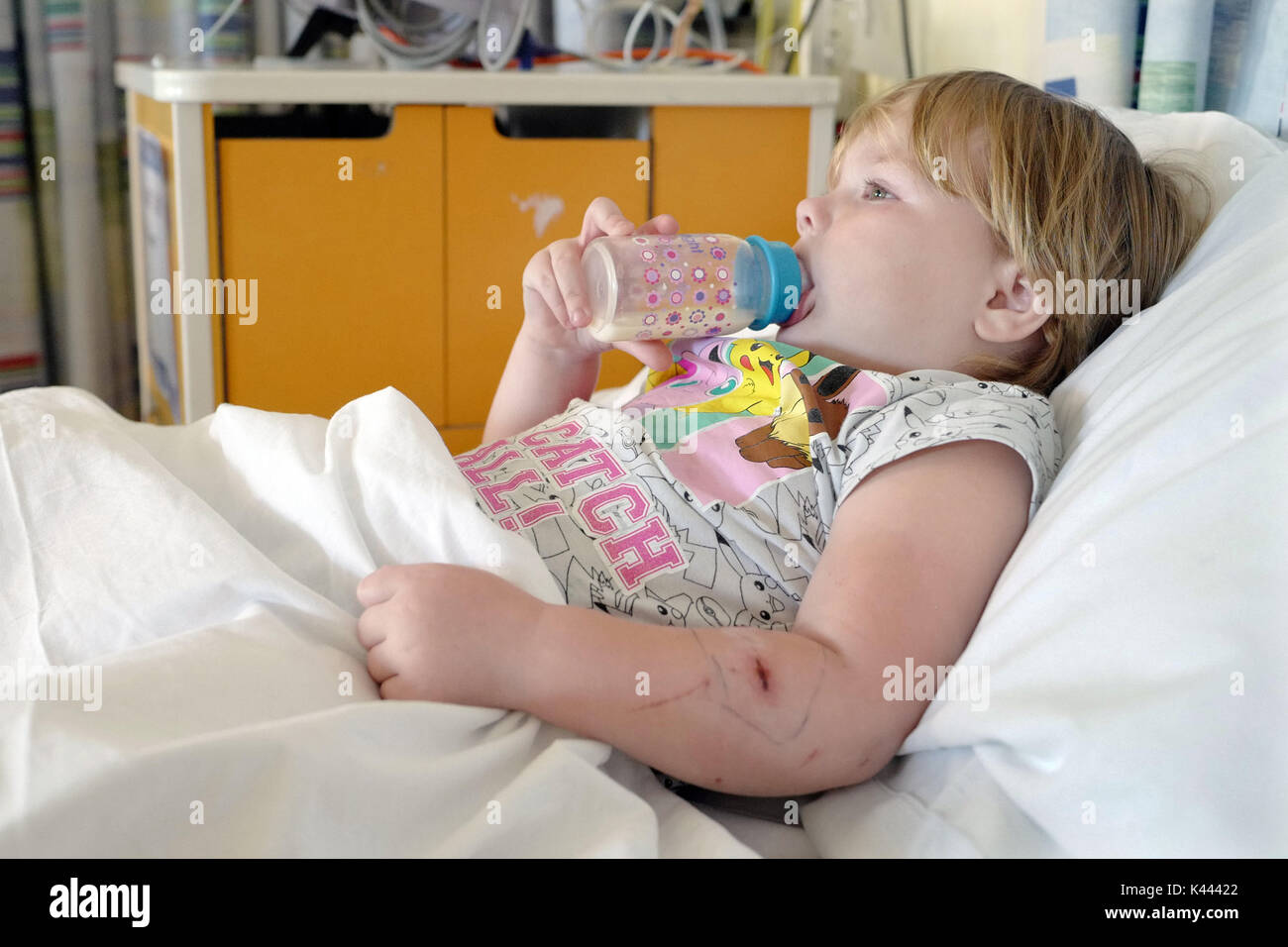 Jeune enfant allongé dans un lit d'hôpital buvant de sa bouteille. Banque D'Images