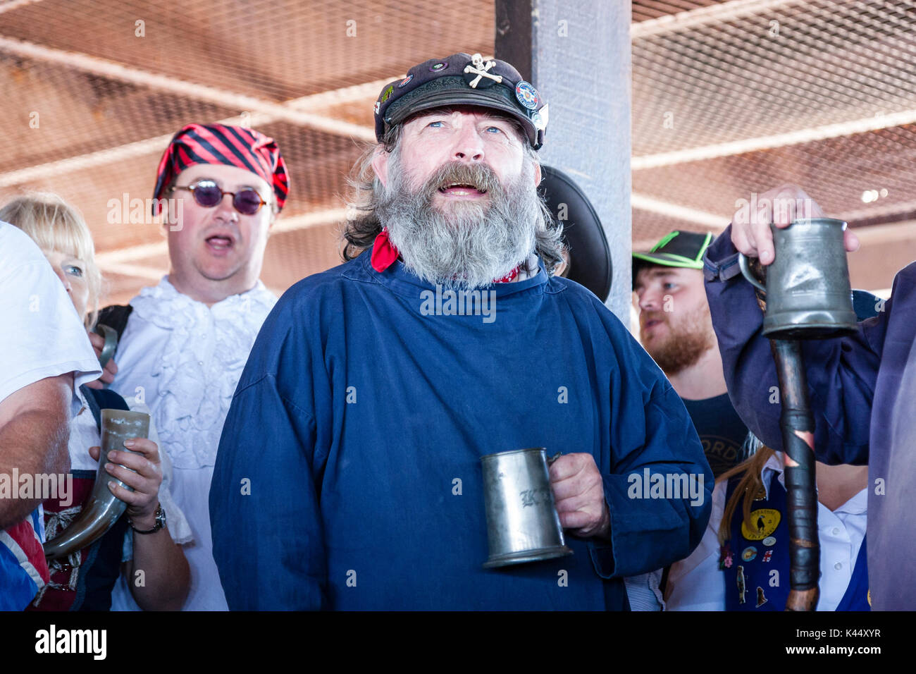 Homme mature avec barbe grise debout, Close up, chantant des chants de marins, tenant une chope de bière, portant le costume de marin du 18ème siècle. Banque D'Images