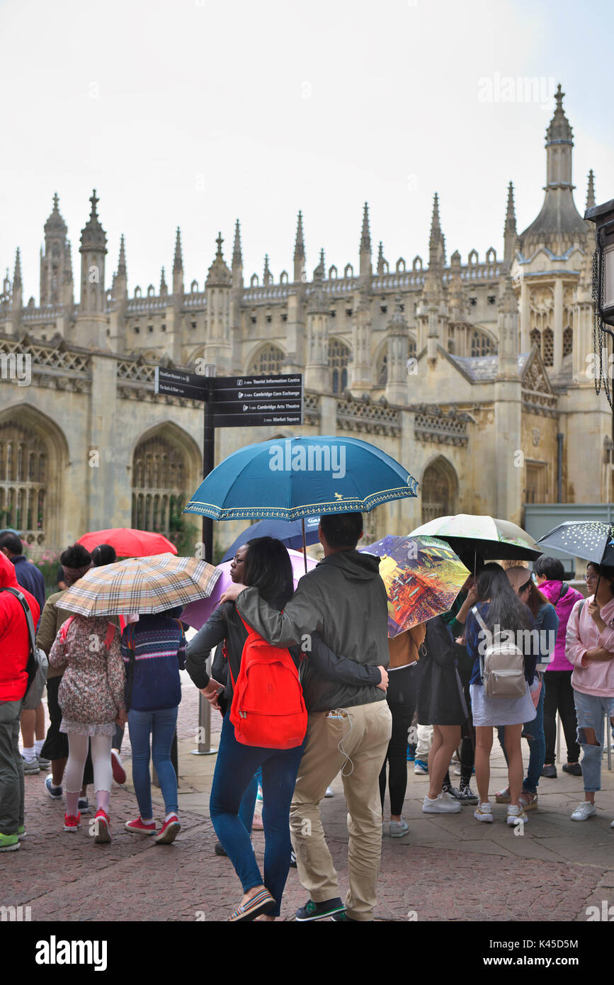 Des groupes de touristes avec un guide réunir en dehors de Kings College à Cambridge avec leurs parasols colorés Banque D'Images