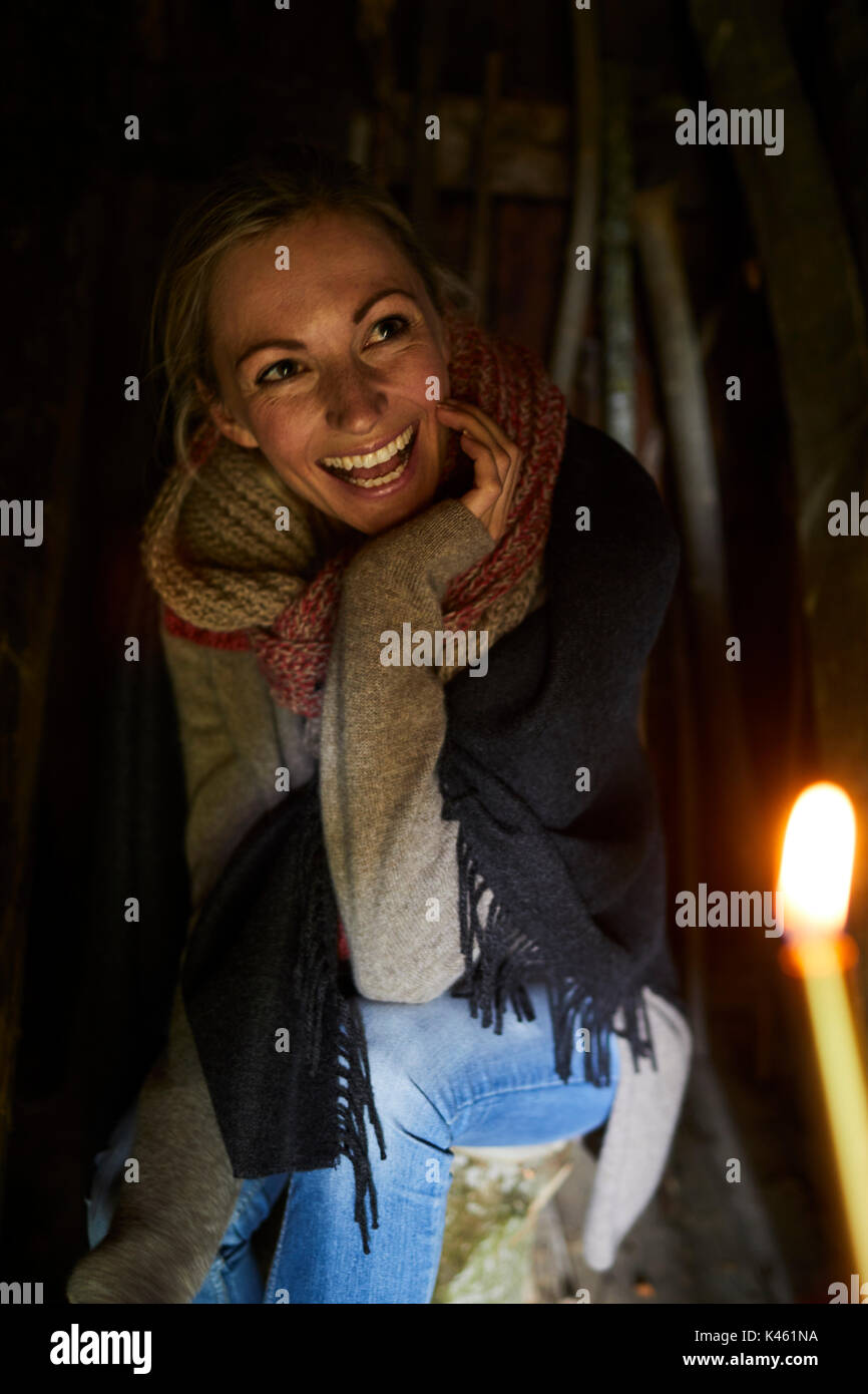 Femme blonde s'asseoir sur un tronc d'arbre, sourire, bougie en premier plan Banque D'Images