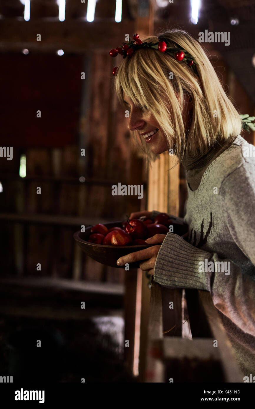 Femme blonde dans une grange, la coiffure, la guirlande avec églantier, bol avec les pommes, side view Banque D'Images