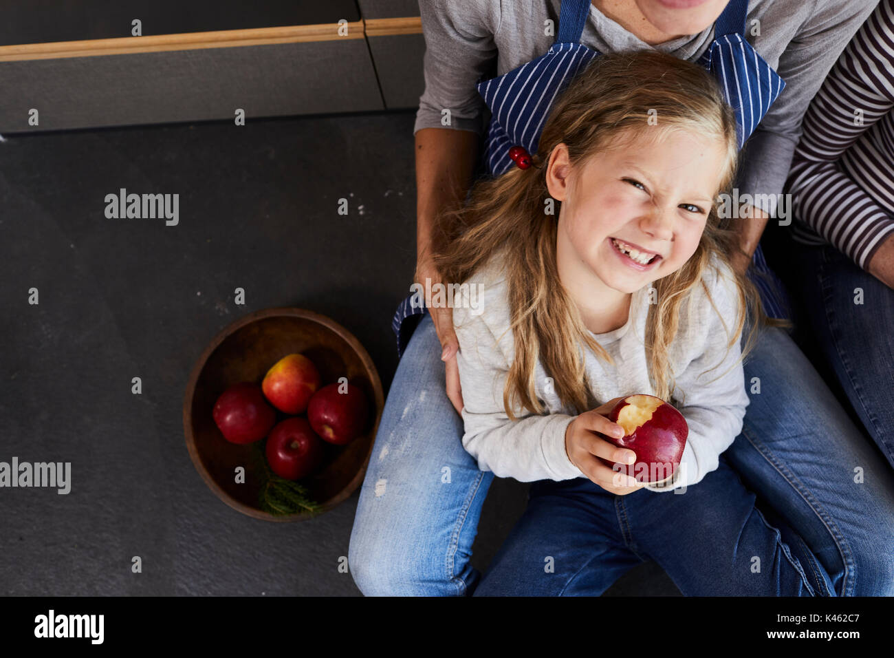 La mère et la fille assis sur plancher de la cuisine, de manger une pomme, à partir de ci-dessus, détail, Banque D'Images