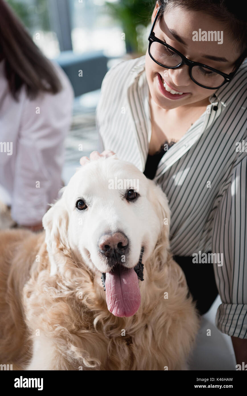 Portrait of young smiling asian woman petting dog in office Banque D'Images