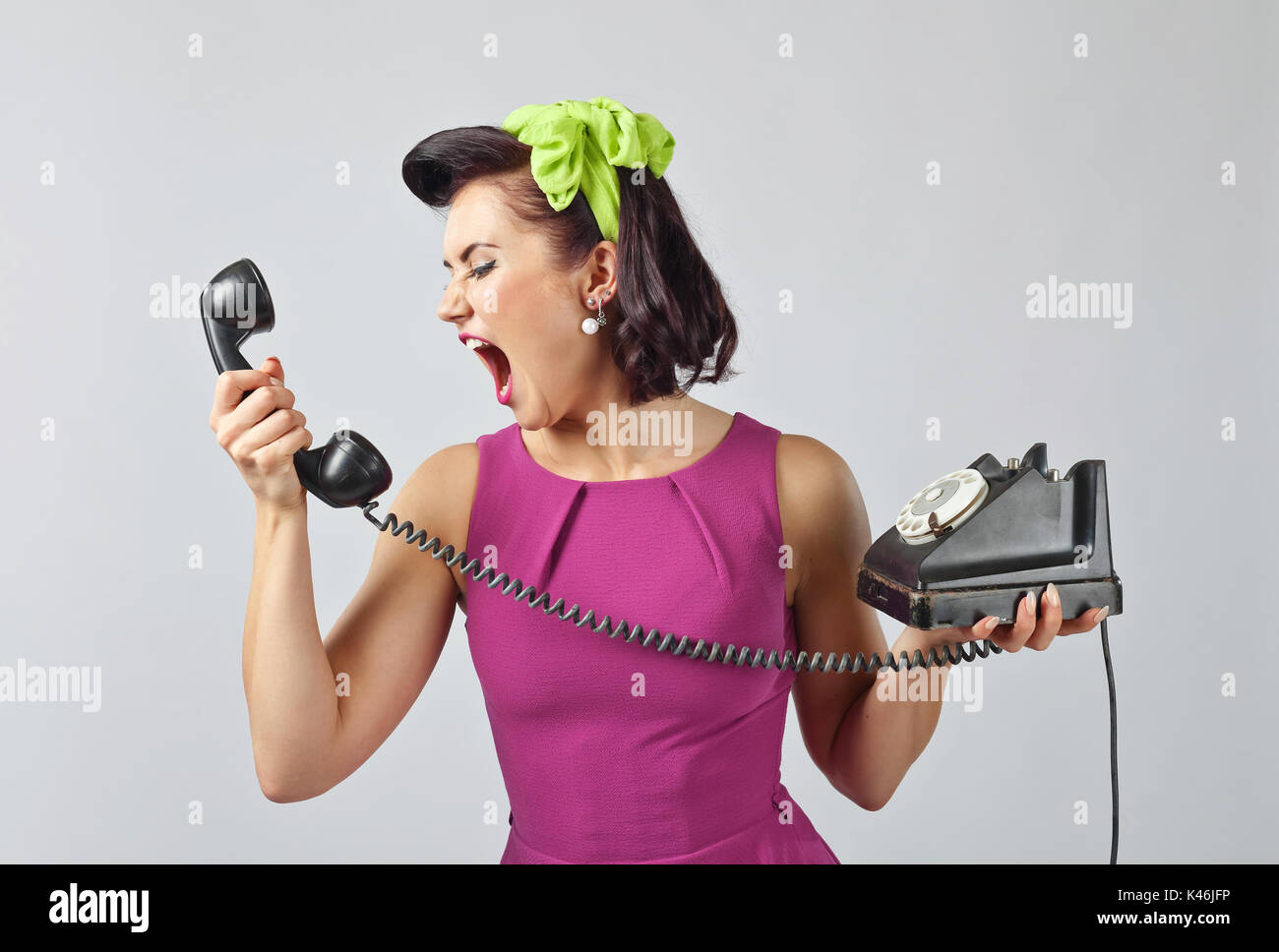 Jeune femme criant à un téléphone .Belle brunette woman in style pin up avec cheveux parfaits et porter la parole via téléphone vintage.facia expressif Banque D'Images