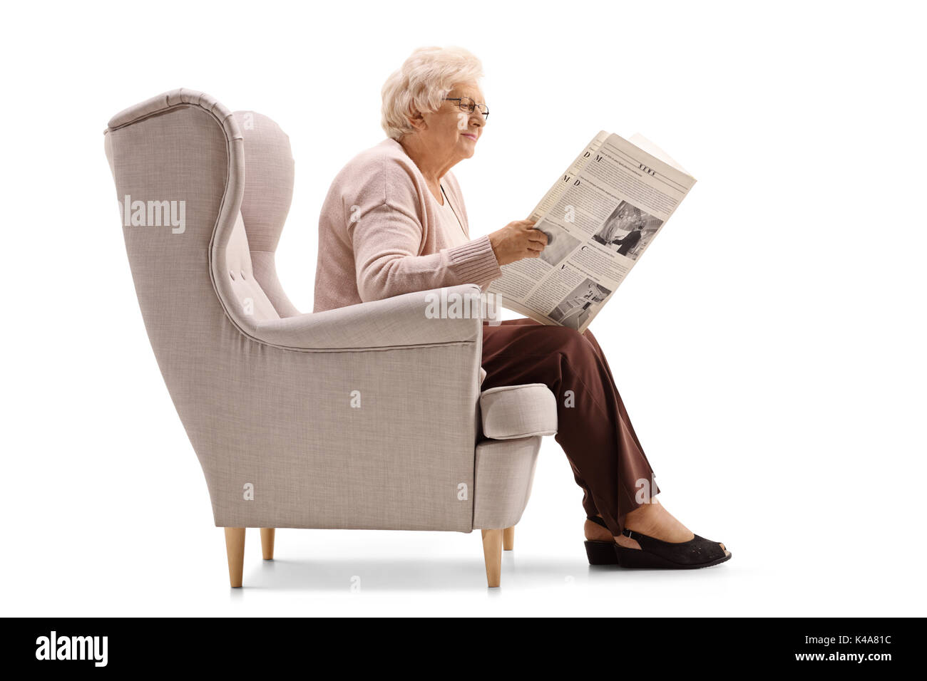 Photo de profil d'une femme mature assise sur un fauteuil et de lire un journal isolé sur fond blanc Banque D'Images