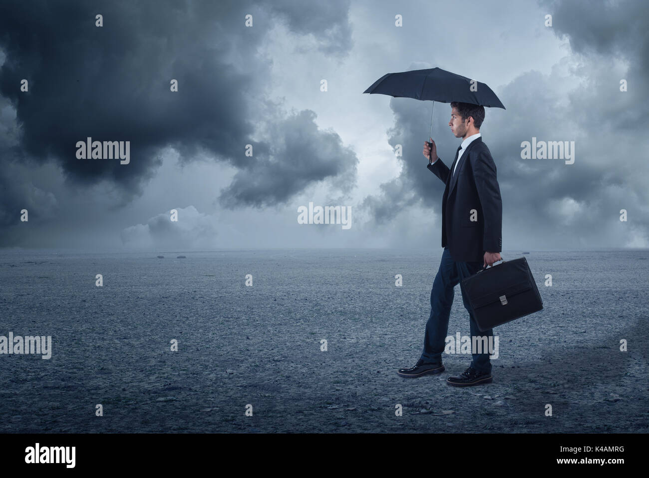 Businessman with umbrella debout à l'arrière-plan nuageux Banque D'Images