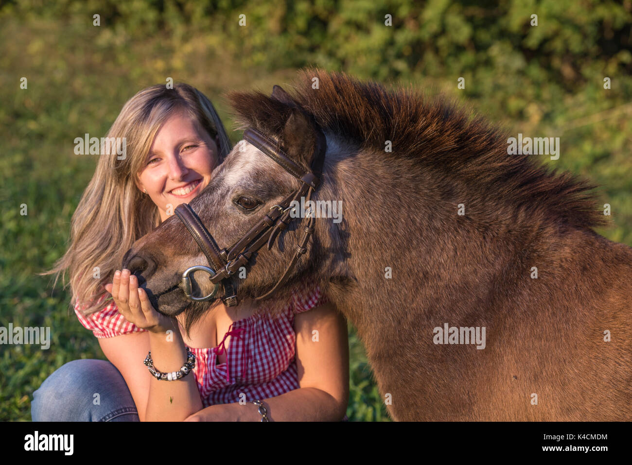 Laughing young blonde woman taquine brown poney shetland en face de végétation verte Banque D'Images