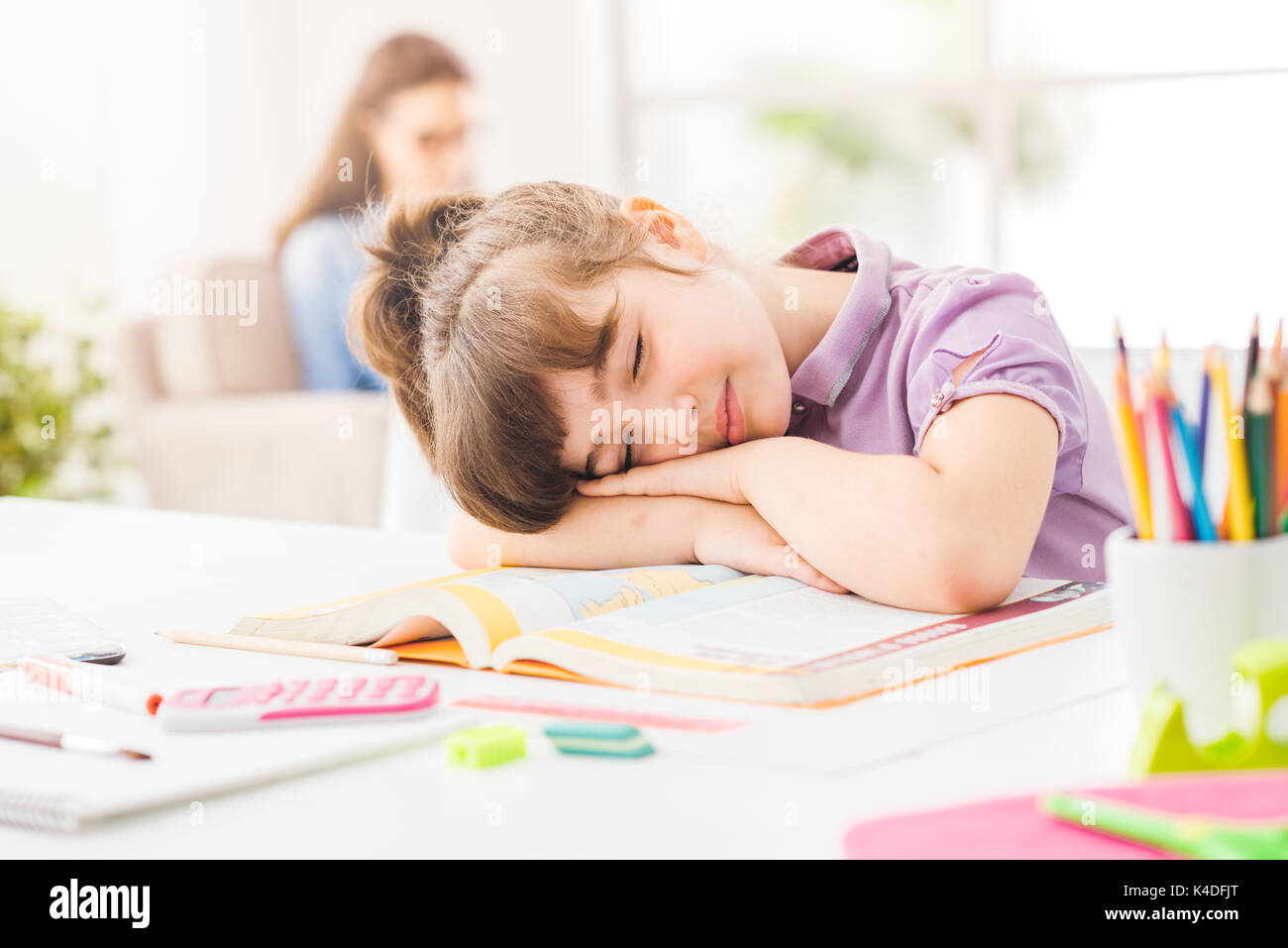 L'élève paresseux girl sleeping sur ses livres, sa mère est assise sur le canapé à l'arrière-plan Banque D'Images