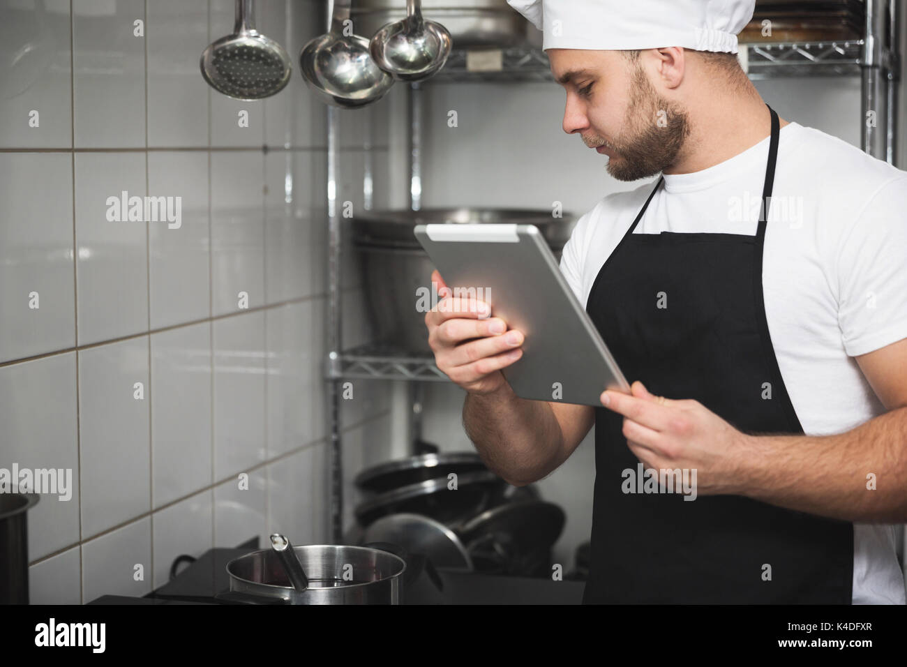 Portrait de côté chef dans la cuisine cuisson de la soupe à l'aide de tablet Banque D'Images