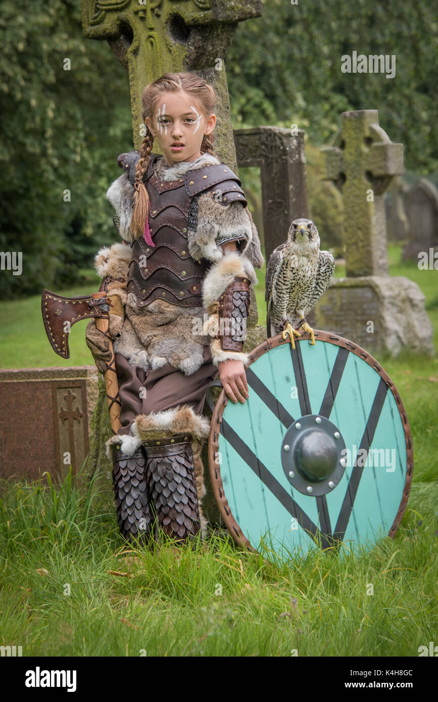 Les jeunes filles vêtues de costumes médiévaux avec hache et d'un faucon de chasse perché sur le garant situé dans un cimetière Banque D'Images