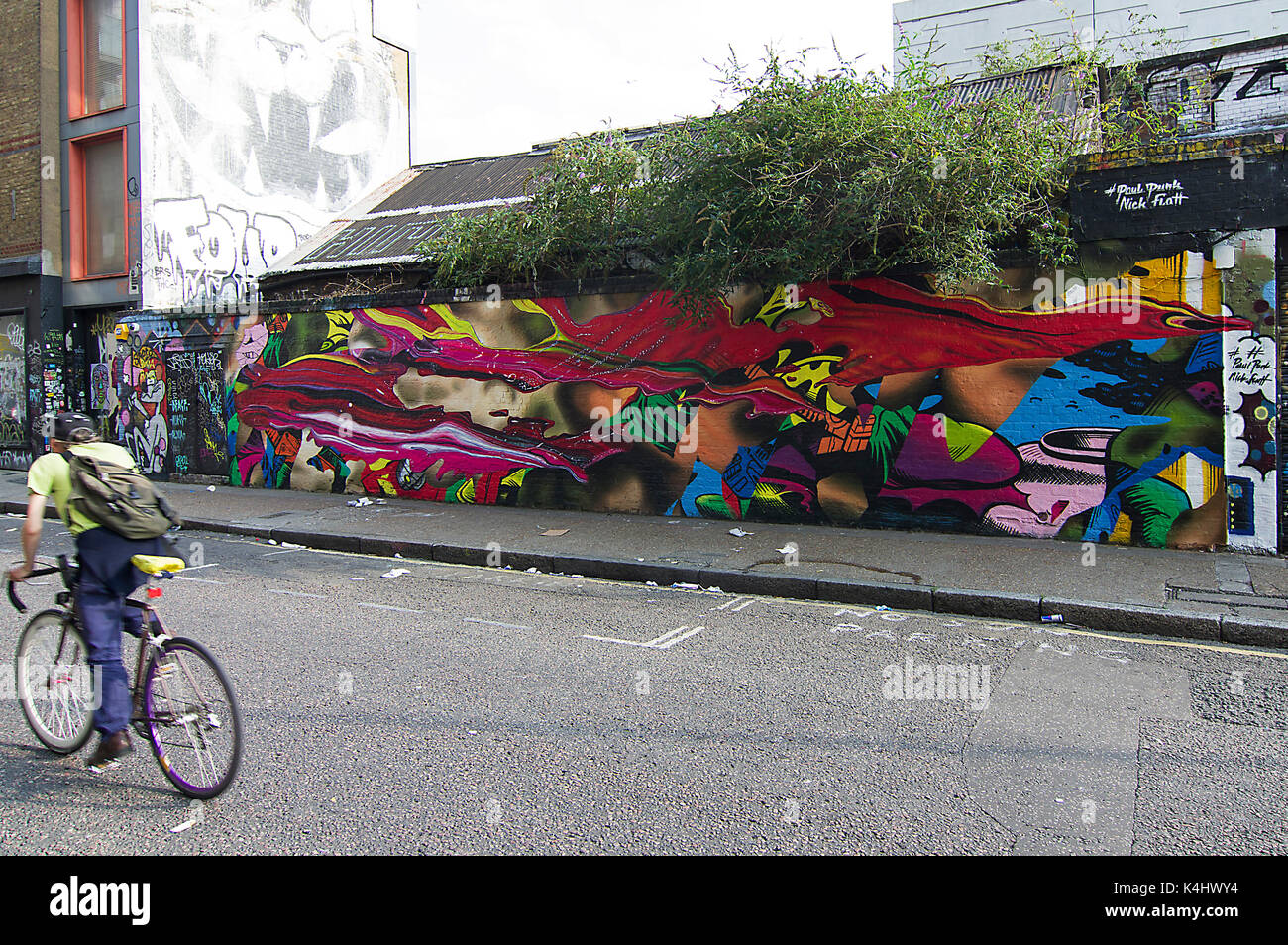 Son visage caché cycliste floue au-delà d'un vélo aux couleurs vives et éclatantes, fresque sur la rue sclater street près de Brick Lane, London, UK Banque D'Images