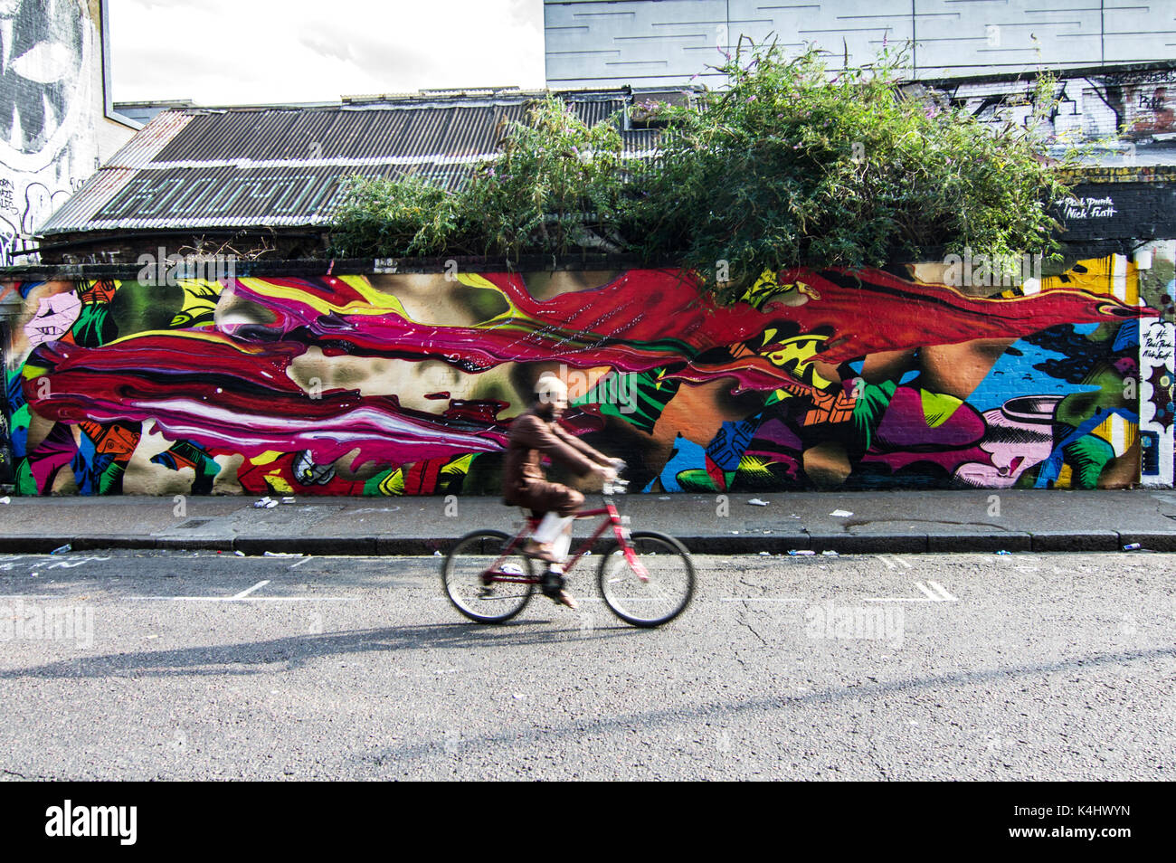 Musulman en brun, le visage brouillé depuis un vélo aux couleurs vives et éclatantes, fresque sur la rue sclater street près de Brick Lane, London, UK Banque D'Images