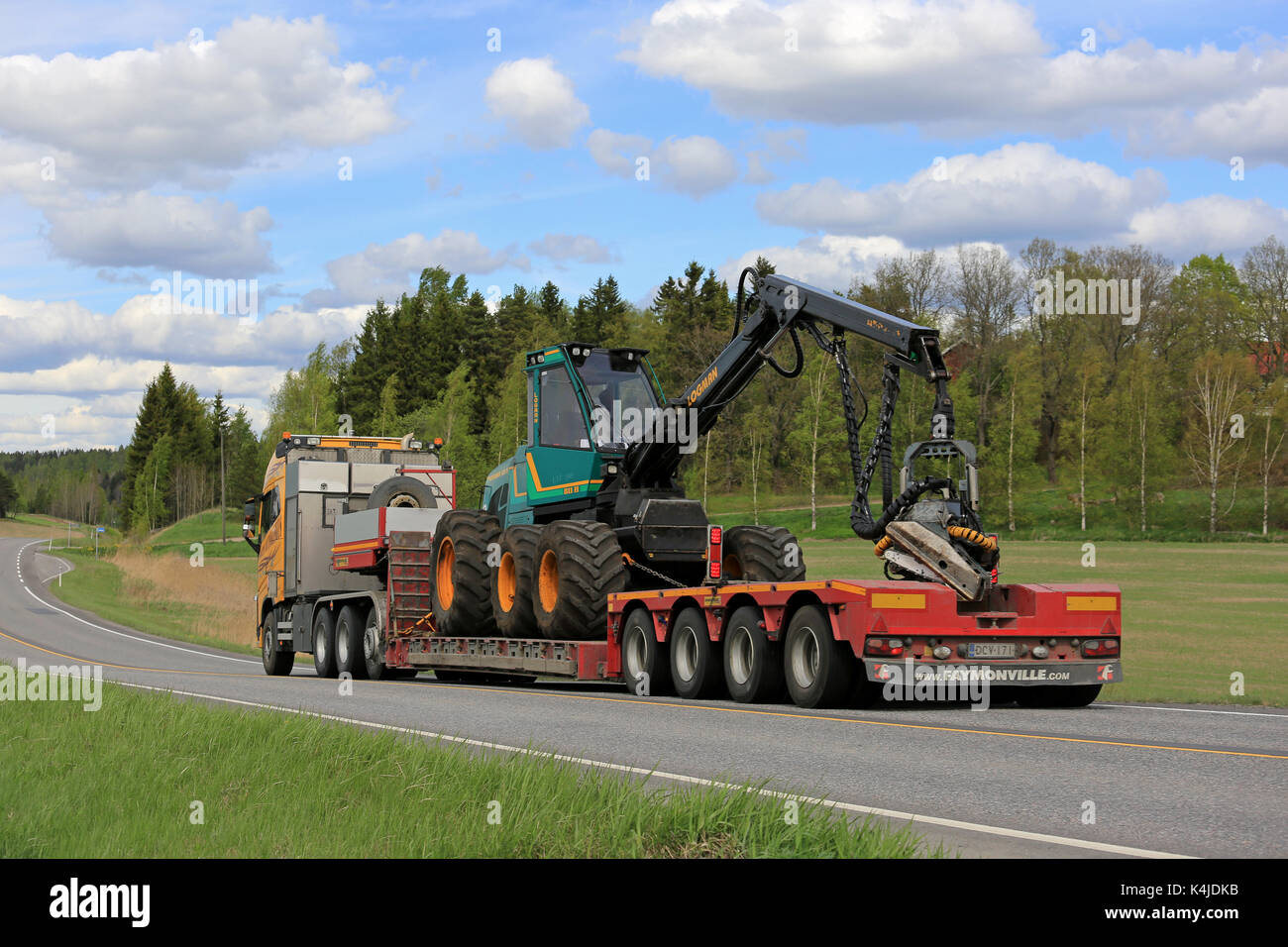 Salo, Finlande - le 25 mai 2017 : Volvo fh jaune de kosken autokeskus logman transporte 811h forest récolteuse sur remorque col de cygne, le long de la route sur un bea Banque D'Images