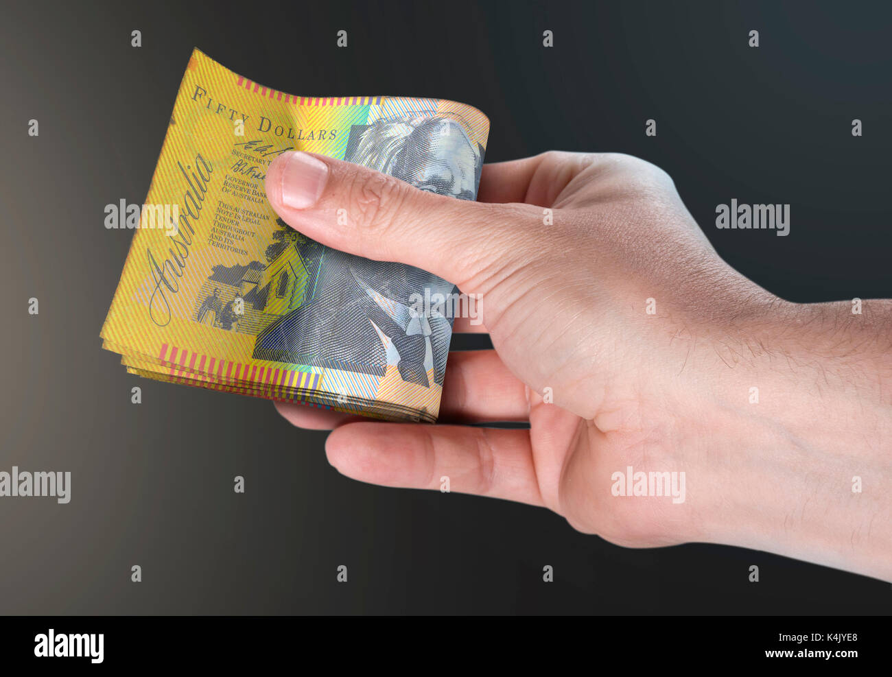 Un homme part remettre une liasse de billets de banque en dollars australiens pliée sur un fond isolé Banque D'Images