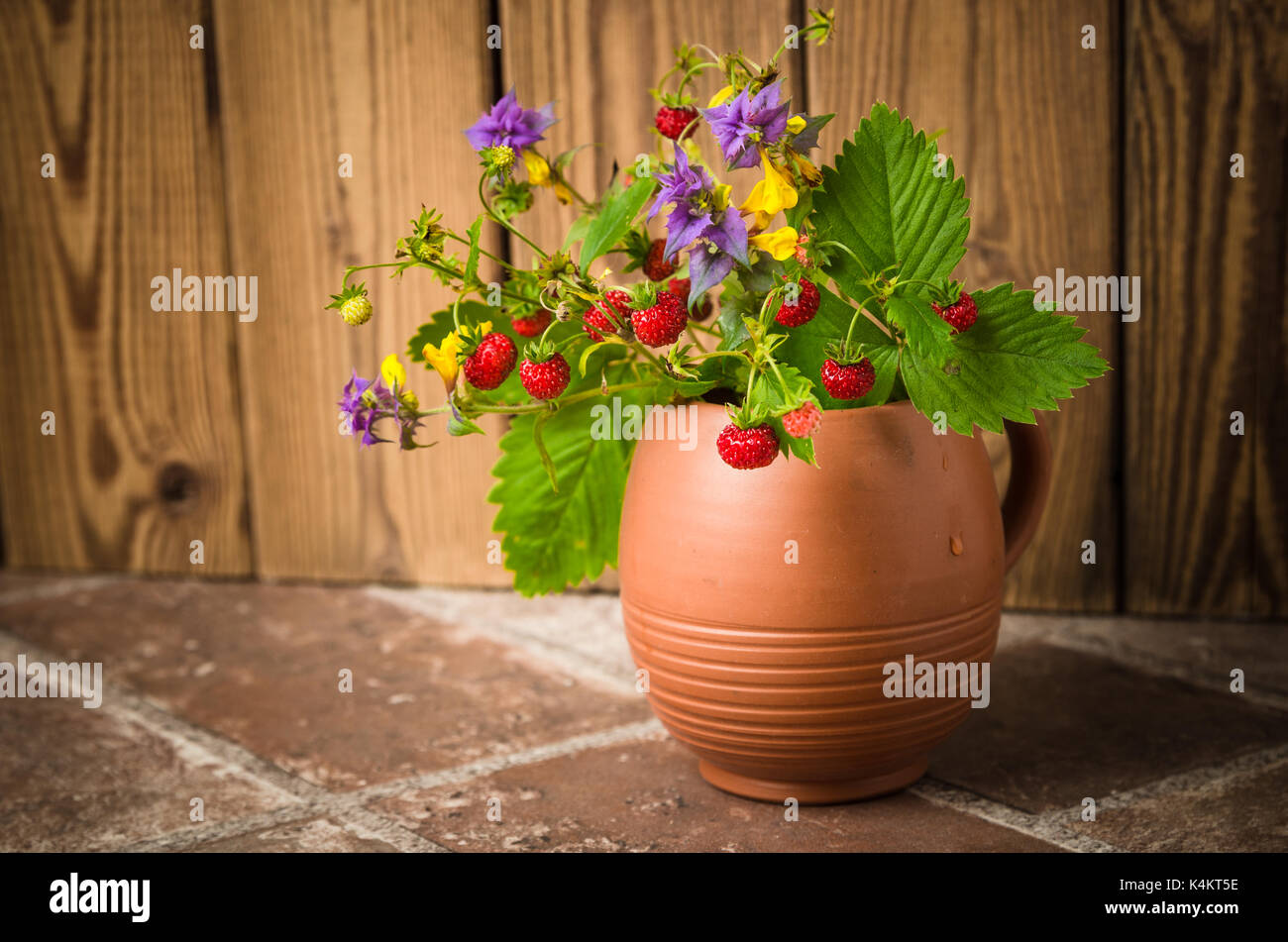Fraise mûre et un bouquet de fleurs de la forêt dans une tasse d'argile Banque D'Images