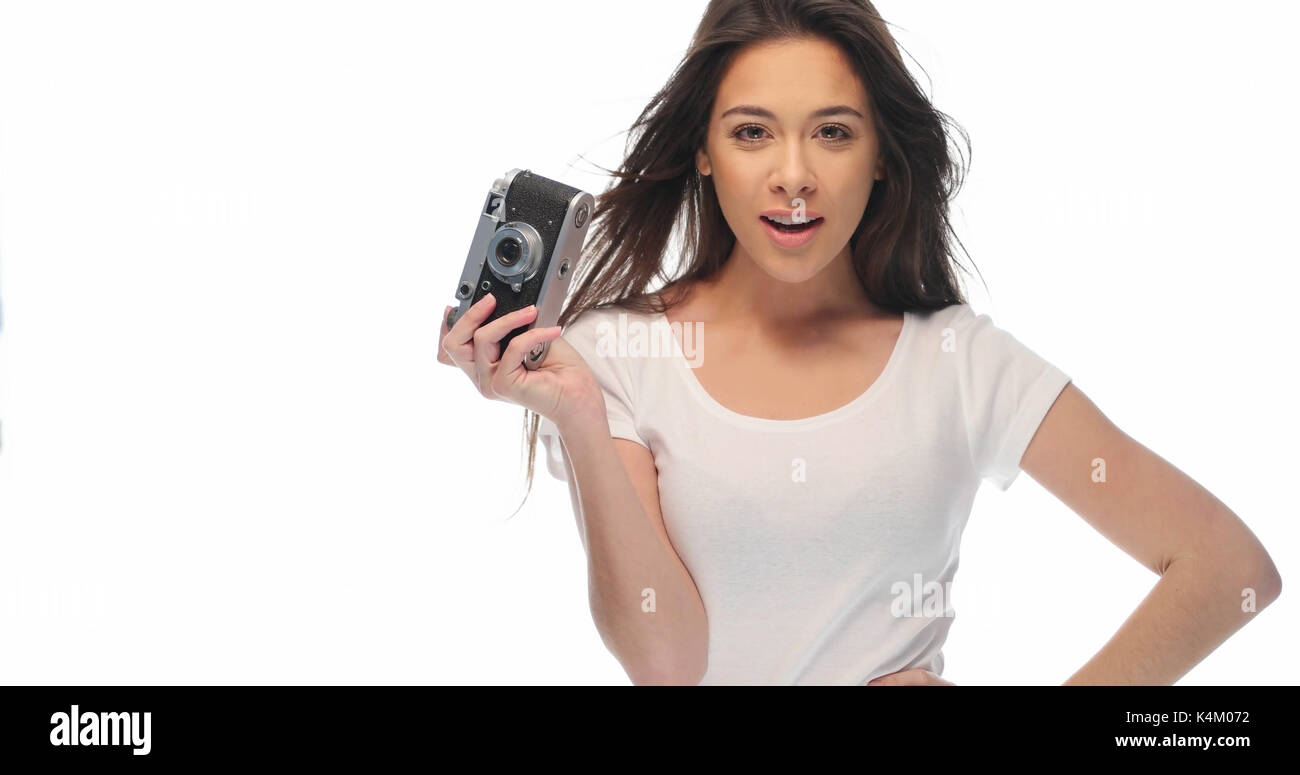 Closeup portrait of pretty young brunette woman in white t-shirt holding retro camera isolated over white background Banque D'Images