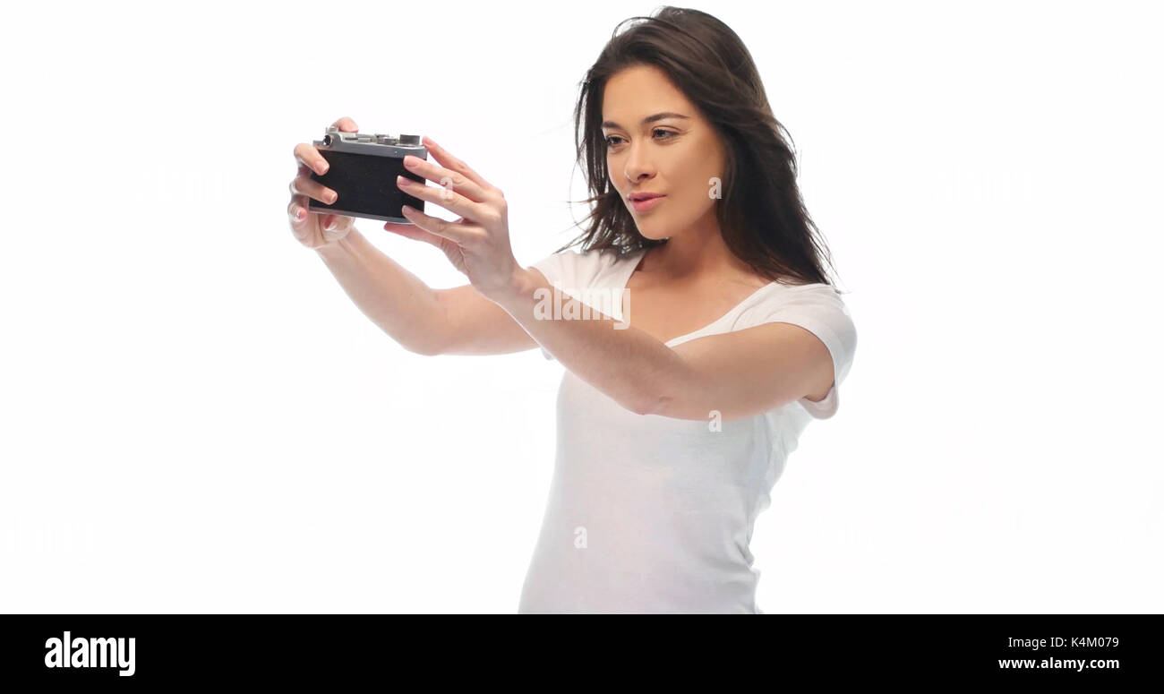Closeup portrait of pretty young brunette woman in white t-shirt holding retro camera isolated over white background Banque D'Images