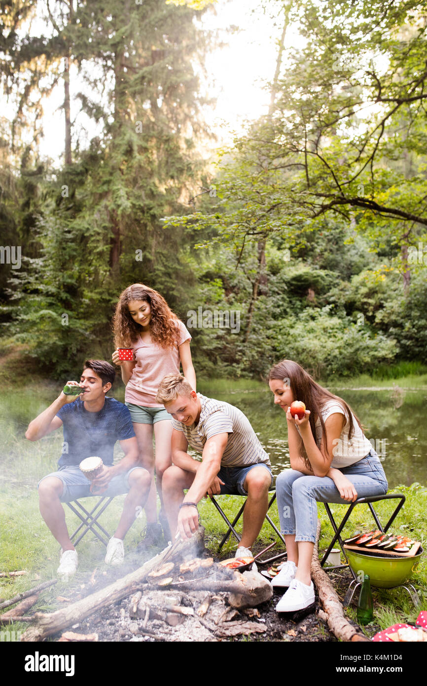 Les adolescents au camping, cuisine viande sur feu de camp. Banque D'Images