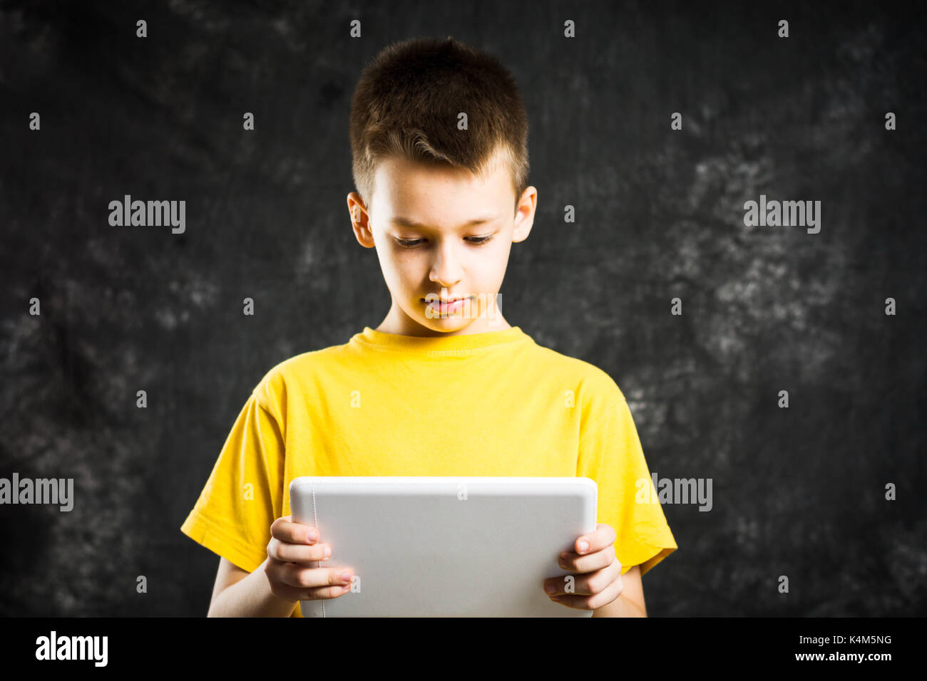 Boy holding a white tablette sur un fond sombre Banque D'Images