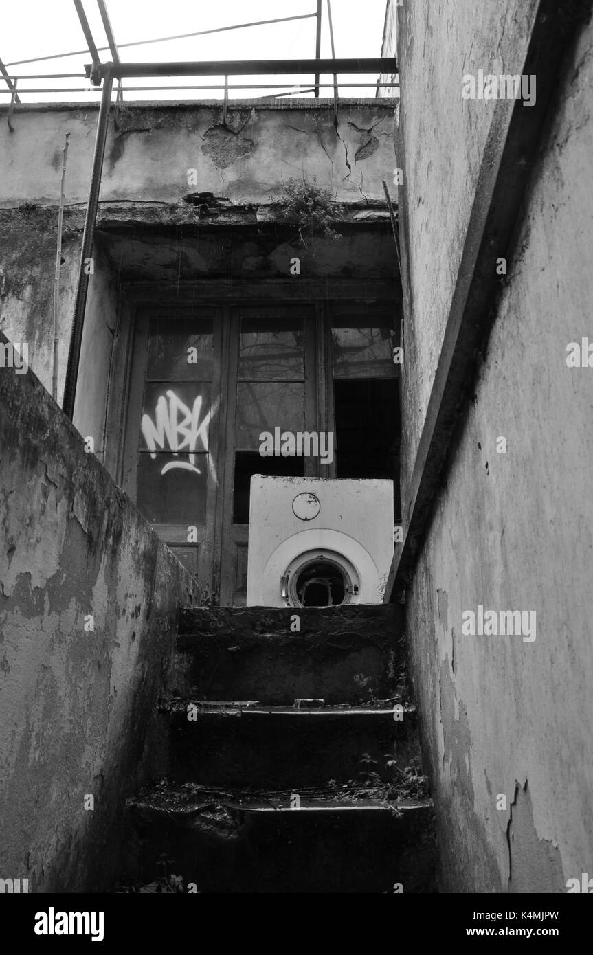 Escaliers de sous-sol et extérieur de maison abandonnée avec un lave-linge sur jour de pluie. Noir et blanc. Banque D'Images