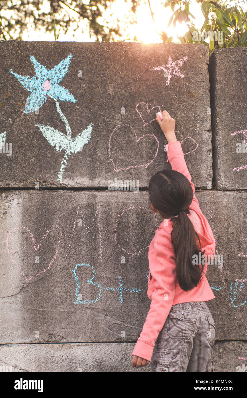 10 ans, petite fille, l'enseignement primaire l'âge, le dessin et l'écriture à la craie sur le béton. Banque D'Images