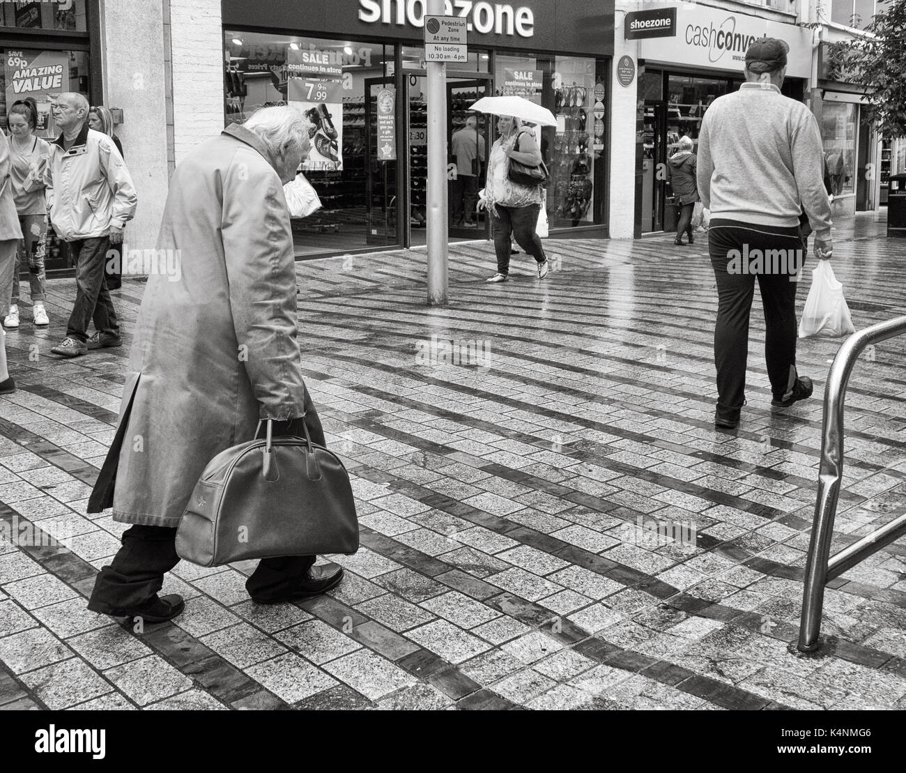 Old man wearing overcoat marche à travers le centre-ville de Leeds au Royaume-Uni. Banque D'Images