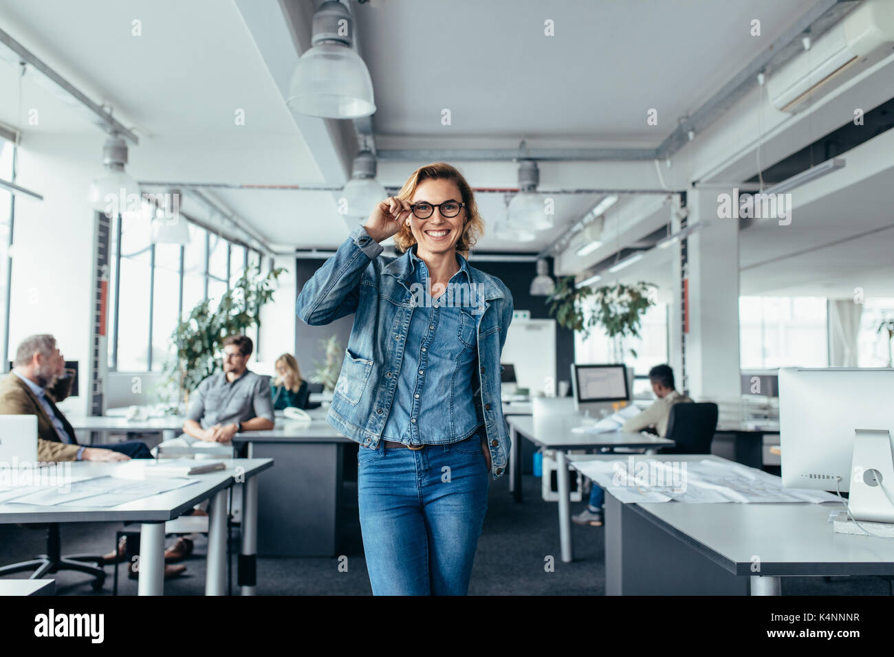 Portrait of smiling businesswoman standing in modern office. Belle jeune femme dans les verres au travail. Banque D'Images