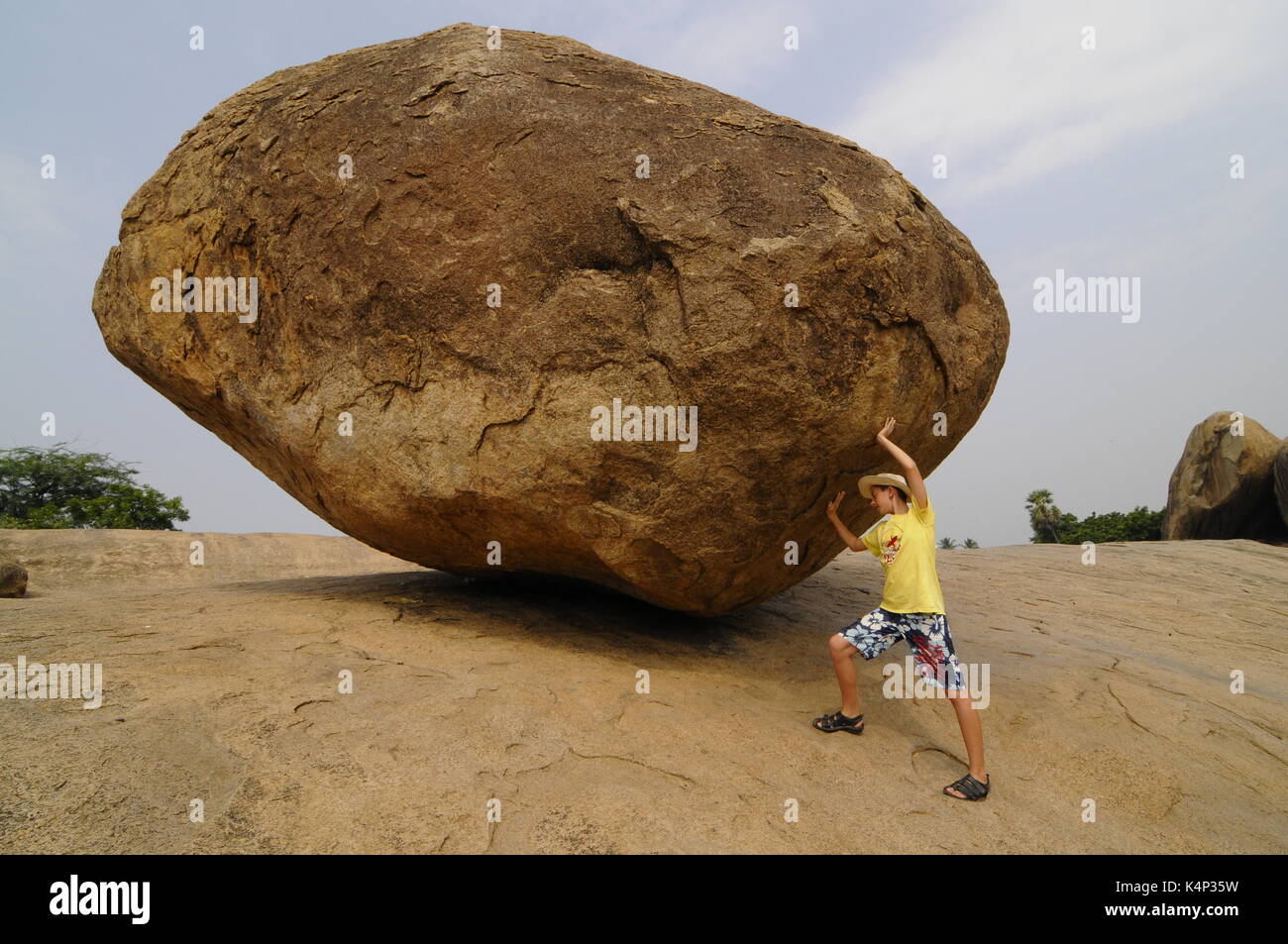 Garçon avec un rocher appelé "Le Seigneur Krishna's butterball', un immense rocher naturel dans le jardin des sculptures à mahabalipuram, Tamil Nadu, Inde, Asie Banque D'Images