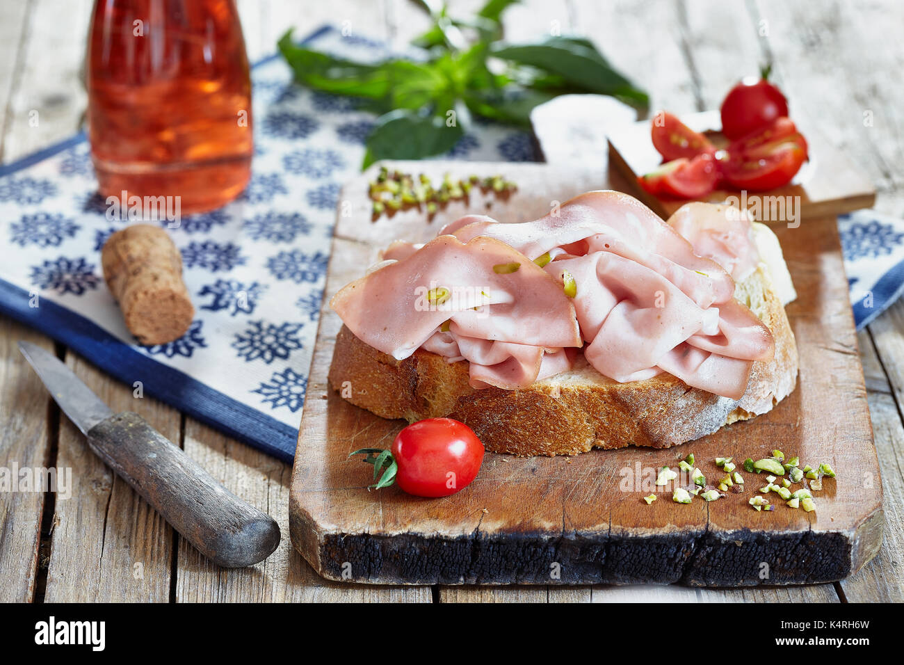 Mortadelle avec les pistaches sur tranche de pain frais, avec des tomates cerise, basilic et rose vin mousseux. Banque D'Images